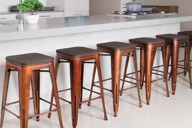 Modern kitchen setting with six copper metal backless kitchen stools with dark wood seats